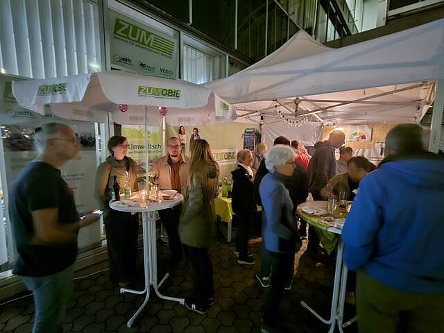 Ca. 10 Personen in mehreren Gesprächsgruppen unter'm Pavillondach vor dem ZUM.