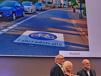 Die drei Genannten mit Urkunde vor einem Foto der Wieslocher Fahrradstraße