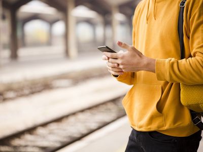 Jugendlicher mit Handy in der Hand am Bahnsteig