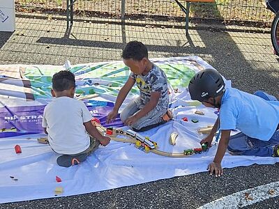 Drei Kinder beim intensiven Spiel mit dem Holzspielzeug auf dem VCD-Bodenbanner
