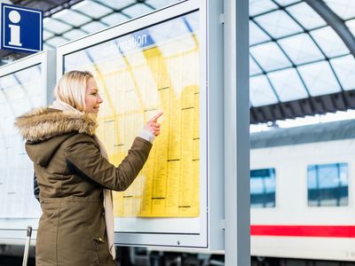 Frau liest Fahrplan am Bahnsteig