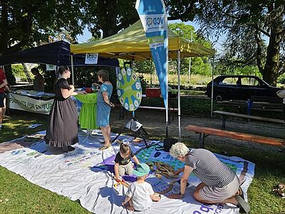 Ältere Dame mit zwei Kindern beim Spiel mit der Holzeisenbhn auf dem VCD-Bodenbanner, im Hintergrund zwei Damen im Gespräch am Glücksrad 