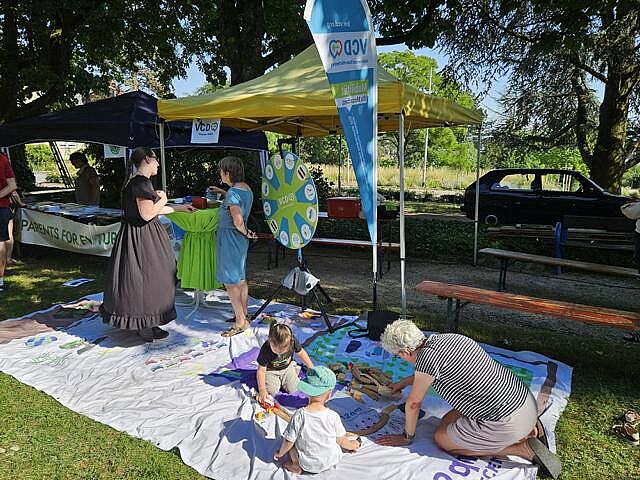 Ältere Dame mit zwei Kindern beim Spiel mit der Holzeisenbhn auf dem VCD-Bodenbanner, im Hintergrund zwei Damen im Gespräch am Glücksrad 