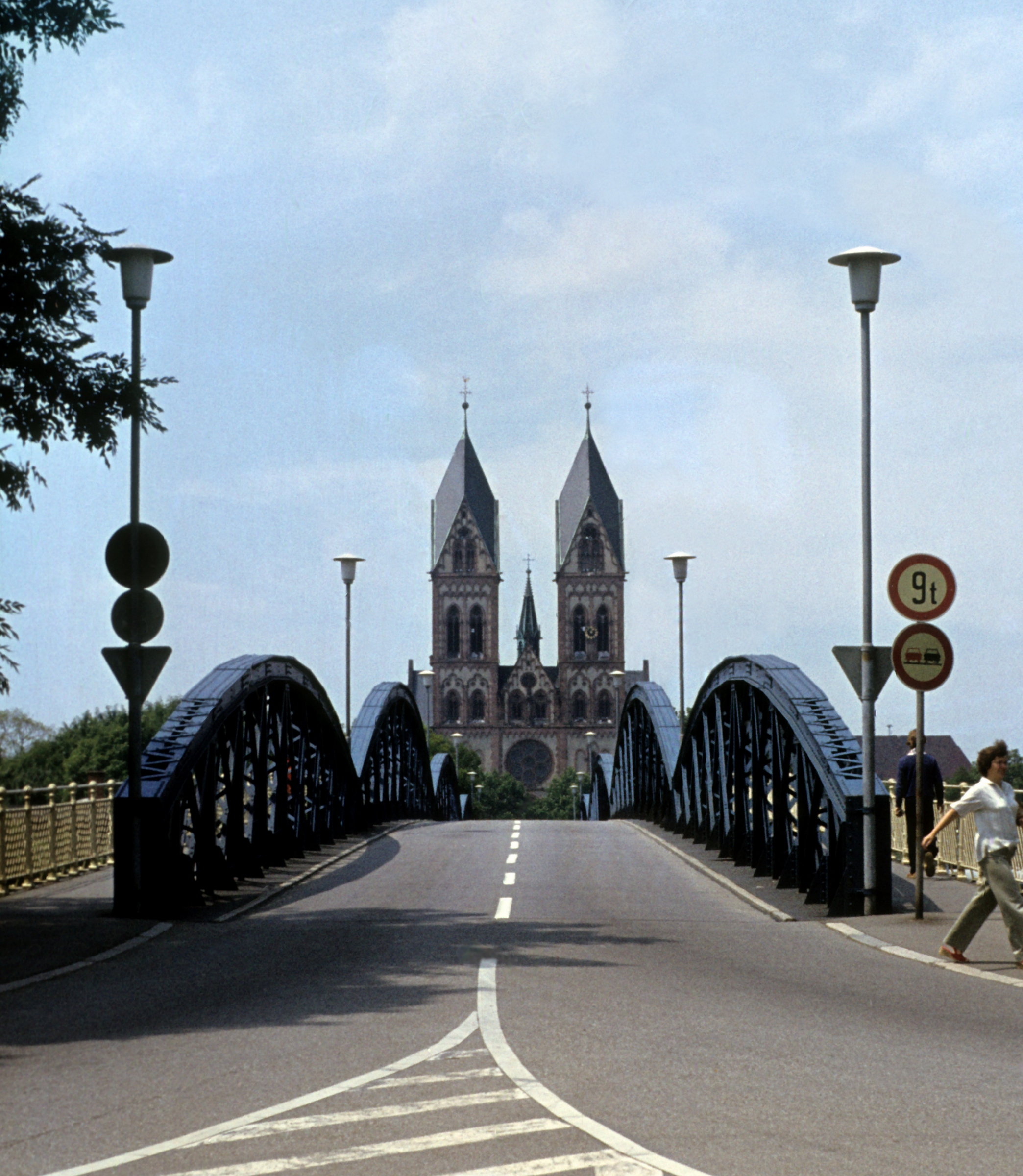 Das Foto zeigt Freiburger Blaue Brücke im Jahr 1980 und ist in Richtung Herz-Jesu-Kirche aufgenommen. Die Fahrbahnmarkierung zeigen eine deutliche Autostraße. Links und Rechts der Fahrbahn sind Verkehrsschilder aufgestellt: Maximal 9 Tonnen und Überholverbot.
